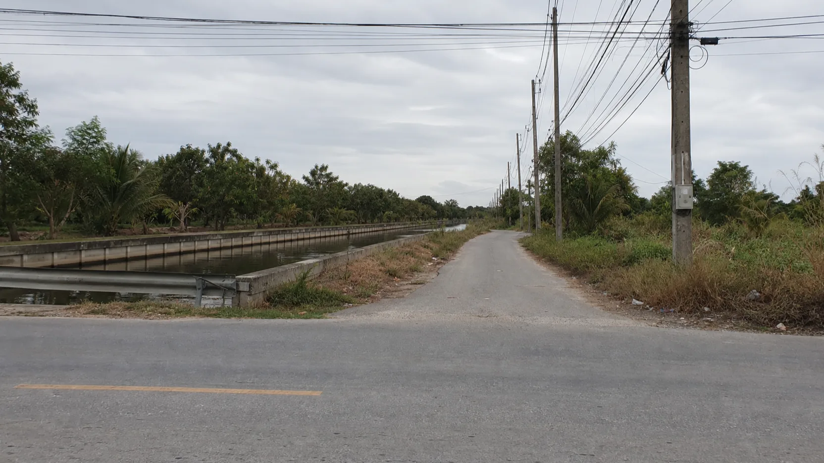 Photograph: the soi off Liap Khlong 4 road at the project entrance — the khlong, the road, the drainage works, honest and unstaged.