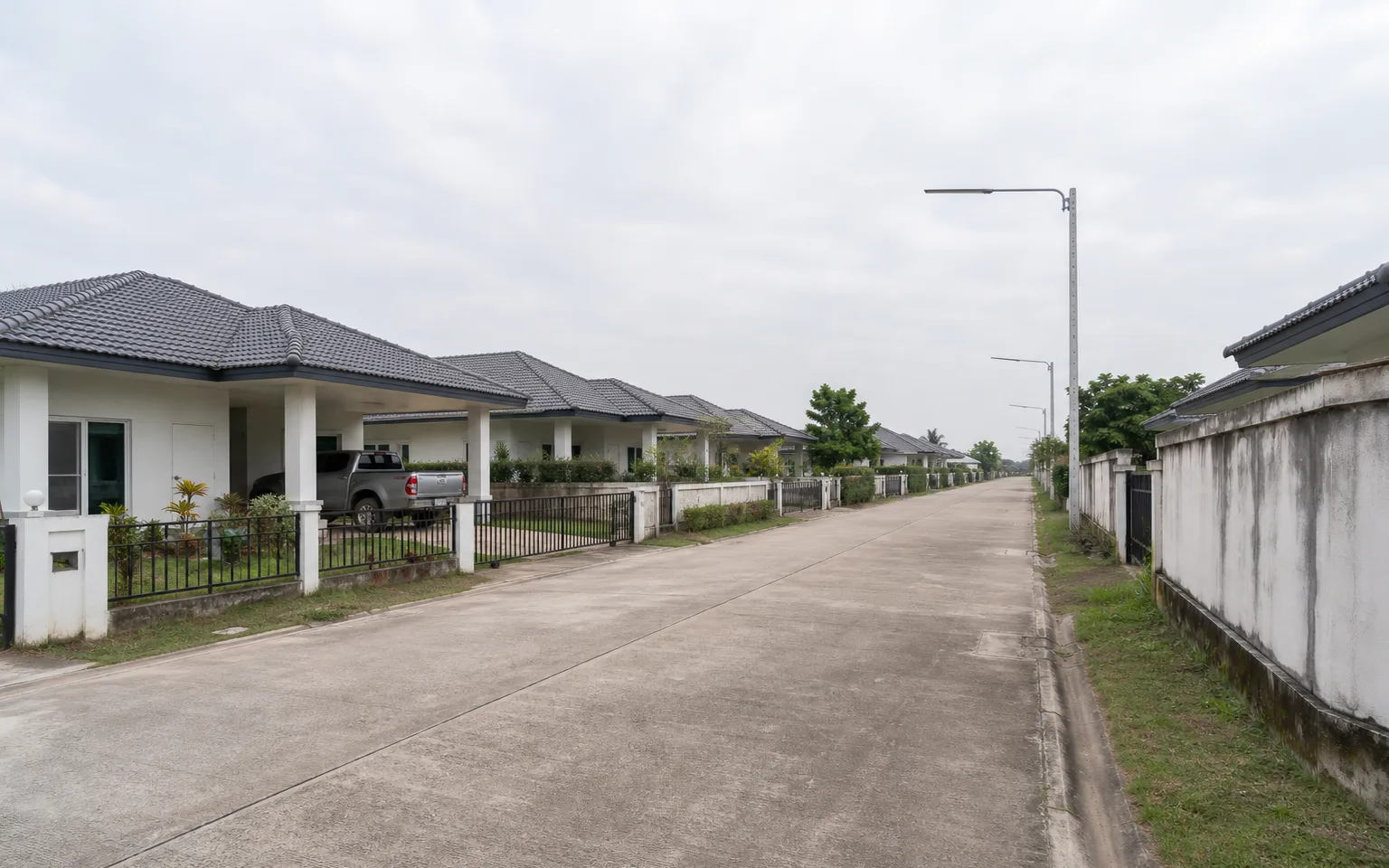 Photograph: a street in Ruensuan Khlong 3, the company's previous project, two years after completion — front gardens filled in, a resident's car in a carport, a boundary wall with two years of weather on it.